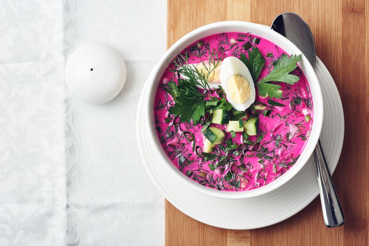 Cold beetroot soup with cucumber, egg and herbs on a  table.