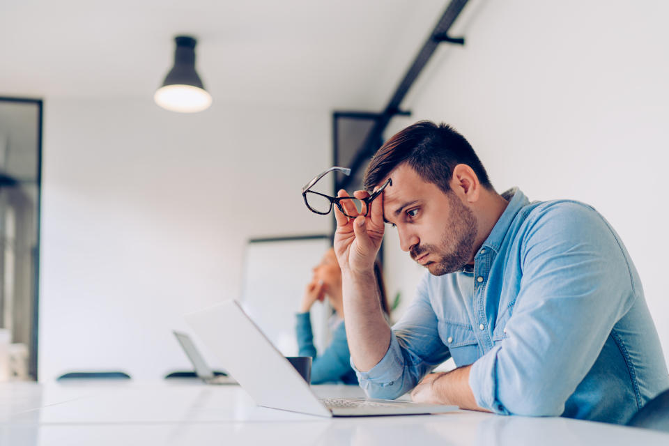 Exhausted young businessman using laptop at work and sitting by the desk while