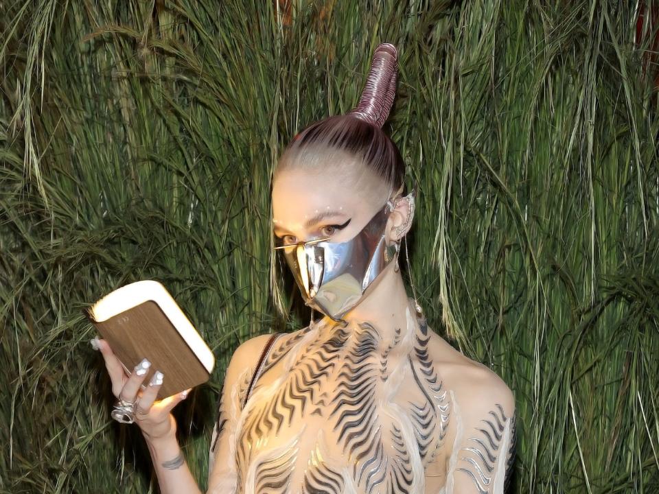 Grimes holding up a book while wearing a science-fiction-inspired costume with a metal mask.