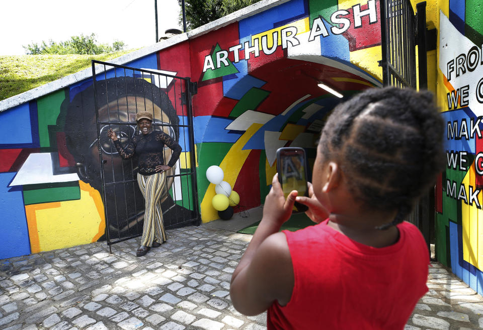 Zimir Jackson, 5, takes a photo of his grandmother Sharron Jackson by the Arthur Ashe tunnel in Battery Park in Richmond, Va., Saturday, June 22, 2019. Groundbreaking black tennis player Arthur Ashe Jr.'s hometown of Richmond, Virginia has renamed a major thoroughfare after him, after years of effort. (Alexa Welch Edlund/Richmond Times-Dispatch via AP)