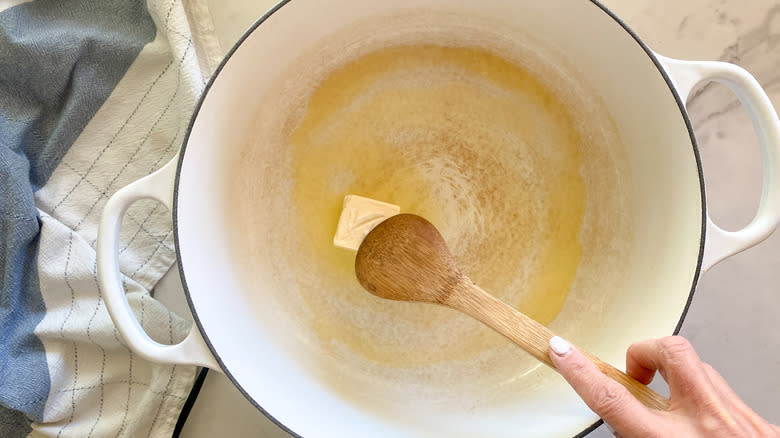 Wooden spoon melting butter in pot.