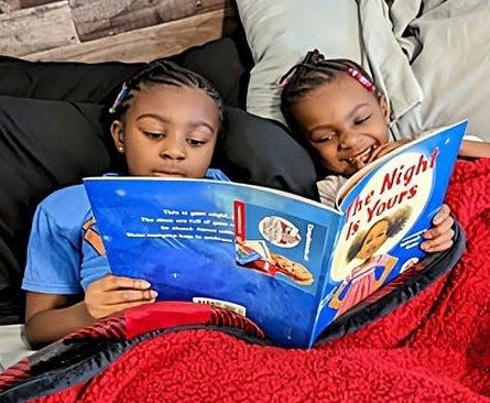 Siblings registered in Dolly Parton's Imagination Library program read a book together.