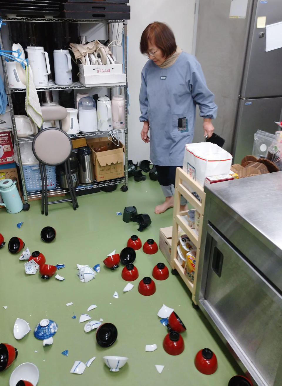 A landlady of a Japanese style hotel stands near damaged bowls following an earthquake in Minamisoma, Fukushima prefecture, northeastern Japan Saturday, Feb. 13, 2021. The Japan Meteorological Agency says a strong earthquake has hit off the coast of northeastern Japan, shaking Fukushima, Miyagi and other areas. (Tomomi Miura/Kyodo News via AP)