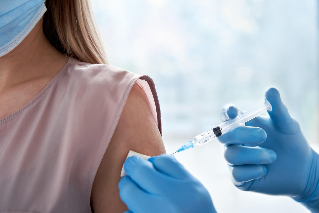 Male doctor holding syringe making covid 19 vaccination injection dose in shoulder of female patient wearing mask. Flu influenza vaccine clinical trials concept, corona virus treatment, close up view.