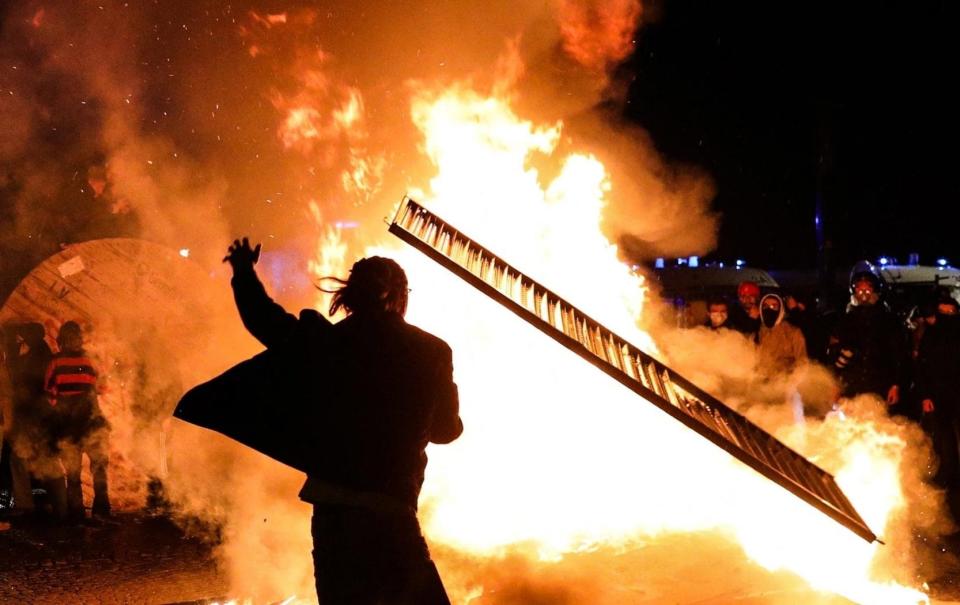 A protester throws a sign depicting Macron onto a huge fire - Frat