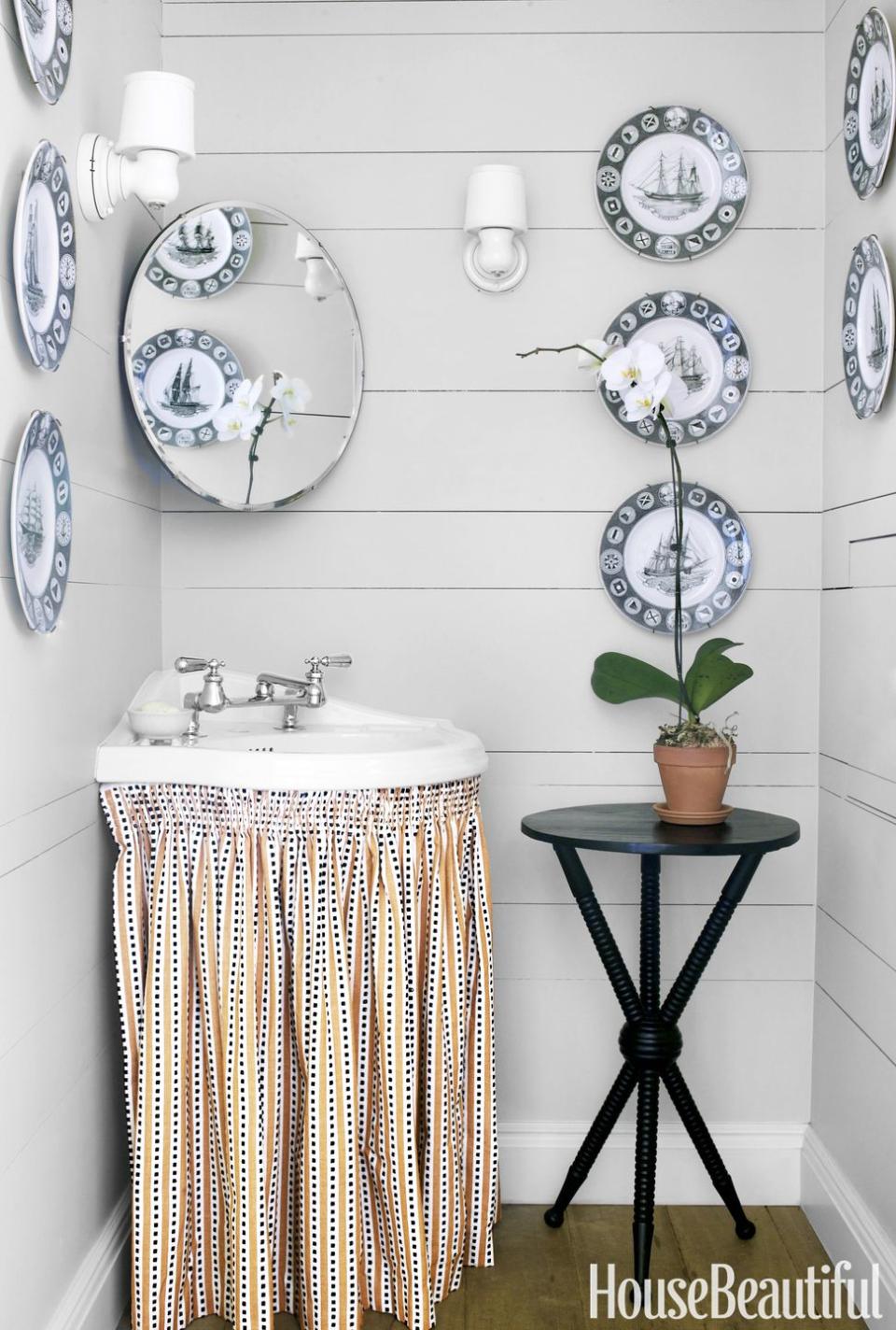 <p>For a powder room this small, a mirror hung at an angle above a corner sink maximizes every inch (and clutter can be stashed behind the fabric skirt). The Wedgwood plates and round accent table help counteract the boxiness, and add charm.</p>