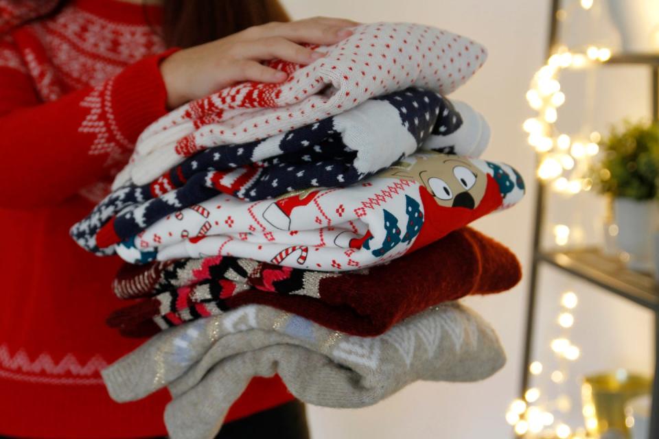 woman holding stack of folded christmas sweaters