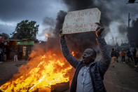 A supporter of presidential candidate Raila Odinga holds a placard referring to electoral commission chairman Wafula Chebukati, while shouting "No Raila, No Peace", next to a roadblock of burning tires in the Kibera neighborhood of Nairobi, Kenya Monday, Aug. 15, 2022. After last-minute chaos that could foreshadow a court challenge, Kenya's electoral commission chairman has declared Deputy President William Ruto the winner of the close presidential election over five-time contender Raila Odinga. (AP Photo/Ben Curtis)