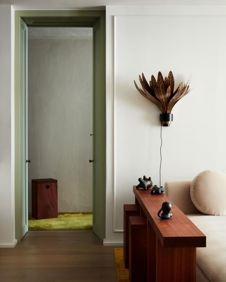 A brass sconce by Dimore Studio anchors this corner of the living room, which also features an elongated side table with modular stools, made to measure by Green River Project. The pottery is from Roman & Williams Guild.