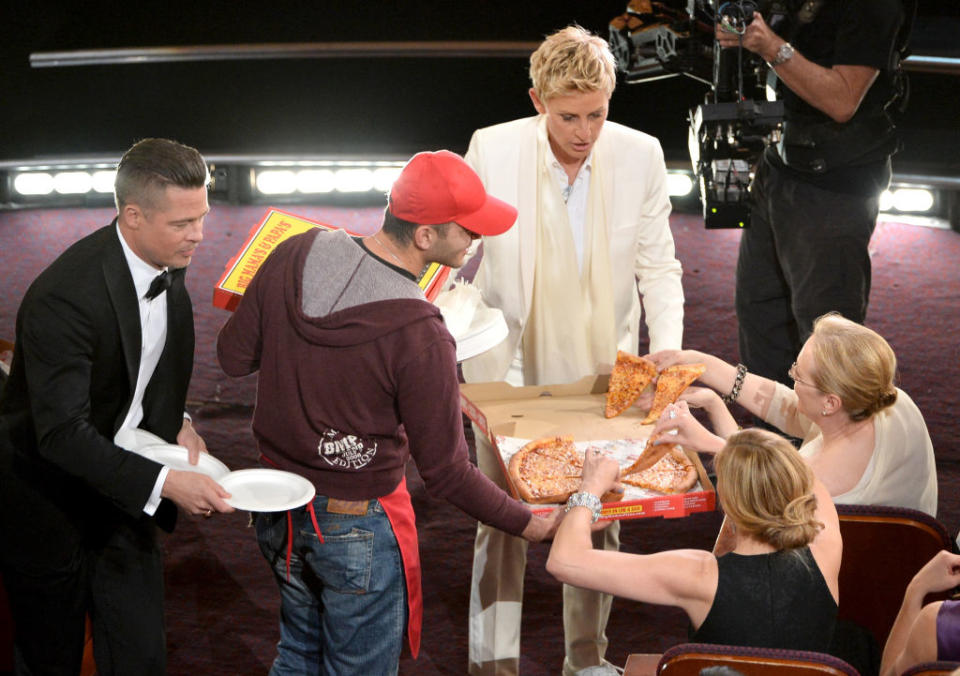 Several people at a formal event taking slices of pizza from delivery boxes held by a pizza delivery person