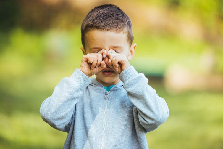 A young boy rubs his eyes.