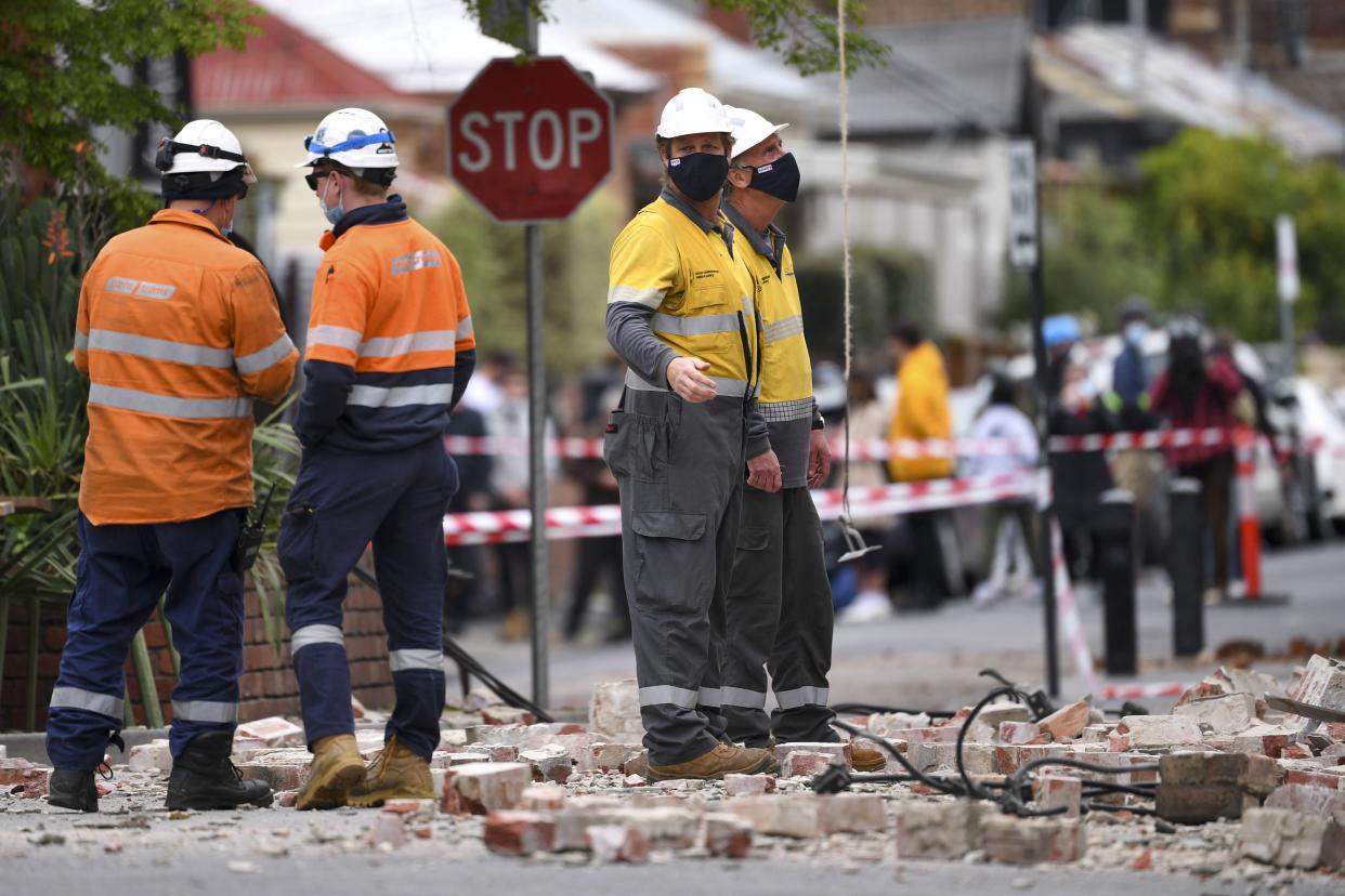 Emergency workers survey damage in Melbourne, Australia, where debris is scattered on a road after part of a wall fell from a building during an earthquake, Wednesday, Sept. 22, 2021. A strong earthquake caused damage in the city of Melbourne in an unusually powerful temblor for Australia, Geoscience Australia said.