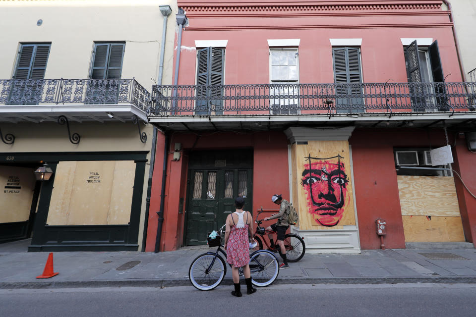 A couple on bicycles stop in front of shuttered businesses impacted by the coronavirus epidemic, on Royal St, in the French Quarter of New Orleans, Tuesday, May 12, 2020. Attempts to curb the spread of COVID-19 have visited a kind of triple economic whammy on the state. (AP Photo/Gerald Herbert)