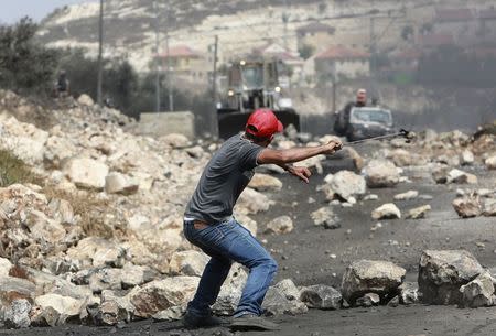 A Palestinian protester uses a sling shot to throw stones towards Israeli troops during clashes following a protest against the nearby Jewish settlement of Qadomem, seen in the background, in the West Bank village of Kofr Qadom near Nablus September 5, 2014. REUTERS/Abed Omar Qusini