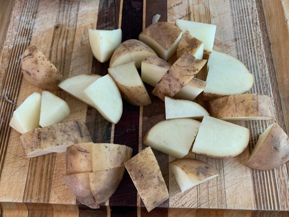 Potato chopped up into cubes on wooden cutting board