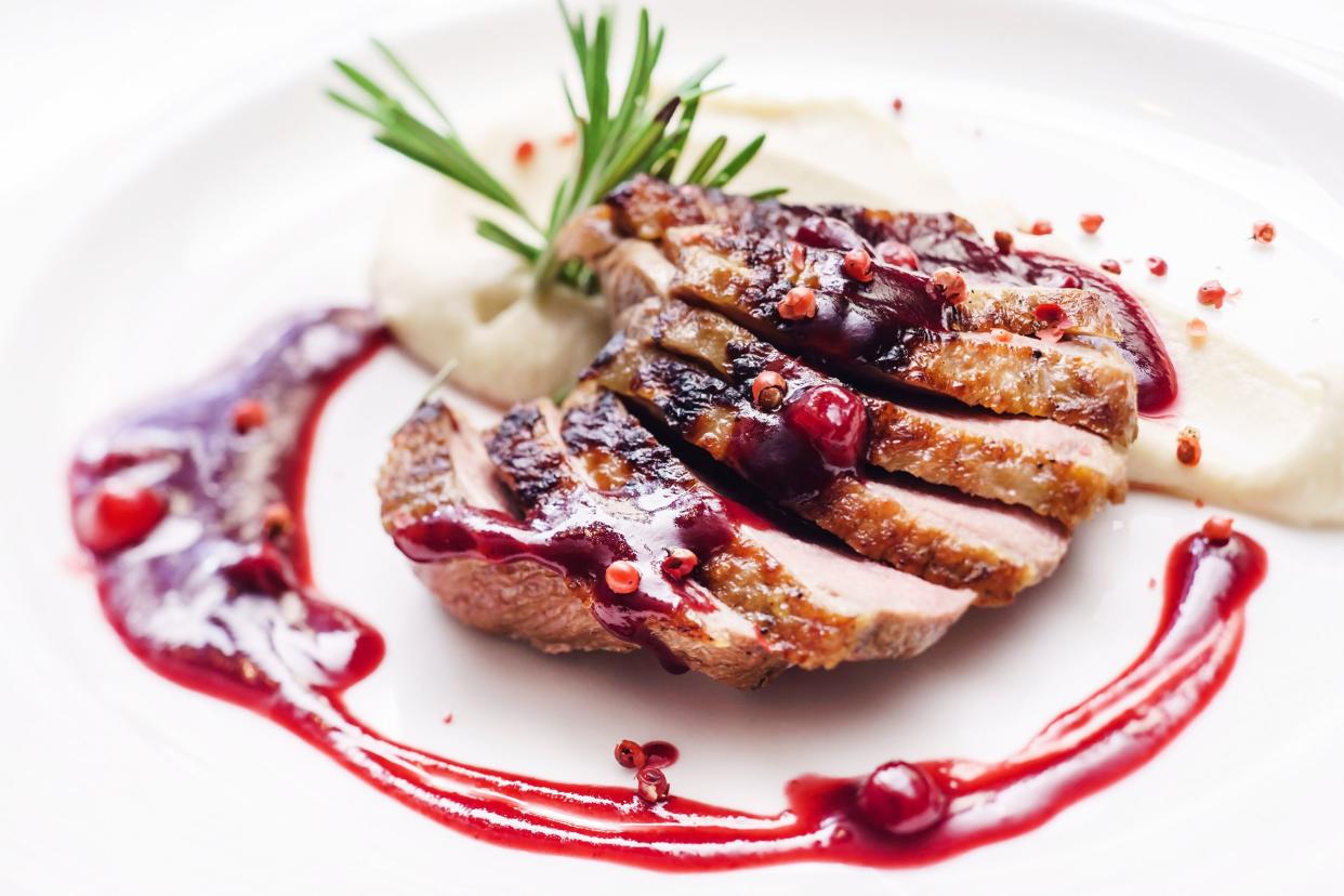 Closeup of duck with cranberry mostaza and garnish on a white plate with a white background
