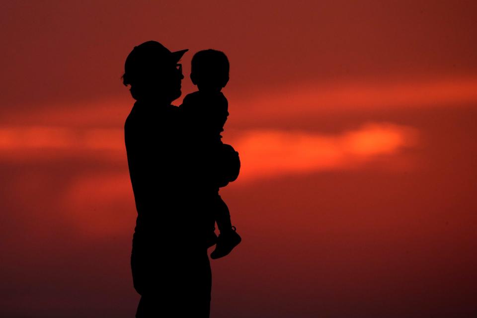 A man and his son are silhouetted against the sky as they watch the sunset from a park in Kansas City, Mo., Friday, June 26, 2020. Sunsets and sunrises were more vibrant than usual lately due to dust in the atmosphere from a Saharan dust cloud.