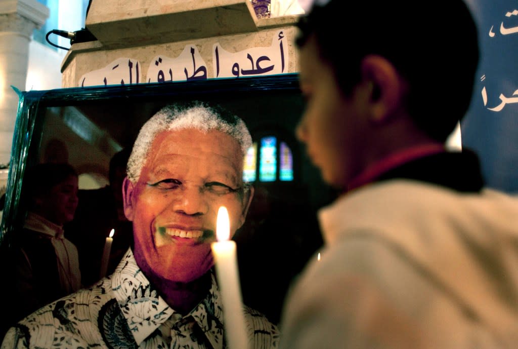 A Palestinian child holds a lit candle as he prays in front of a poster of late South African leader Nelson Mandela, during a special service in his honor at the Holy Family Church, in the West Bank city of Ramallah, Sunday, Dec. 8, 2013. (AP Photo/Nasser Nasser, File)