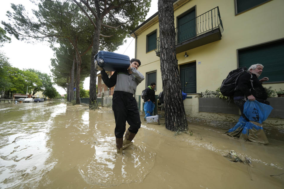 A man carries a suitcase in a flooded road of Faenza, Italy, Thursday, May 18, 2023. Exceptional rains Wednesday in a drought-struck region of northern Italy swelled rivers over their banks, killing at least eight people, forcing the evacuation of thousands and prompting officials to warn that Italy needs a national plan to combat climate change-induced flooding. (AP Photo/Luca Bruno)
