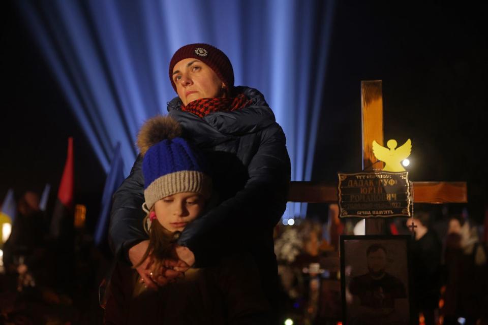 LVIV, UKRAINE - FEBRUARY 23: Iryna Dadak, widow of Yuriy Ruf, stands with her daughter Kateryna, 7, at his grave in the Field of Mars cemetery where hundreds of Ukrainian soldiers who have died in the fighting are buried during a commemoration event with a light installation to mark the first anniversary of Russia's war against Ukraine on February 23, 2023 in Lviv, Ukraine. Ruf, whose real name was Yuriy Romanovych Dadak, was a Ukrainian poet, publisher and screenwriter, and founder of the conceptual literary project "Spirit of the Nation", which influenced nationalist currents in Ukraine. He was a member of the 24th Brigade of the King Danylo Armed Forces of Ukraine and was killed in April of 2022. Russia invaded Ukraine on February 24, 2022. (Sean Gallup/Getty Images)