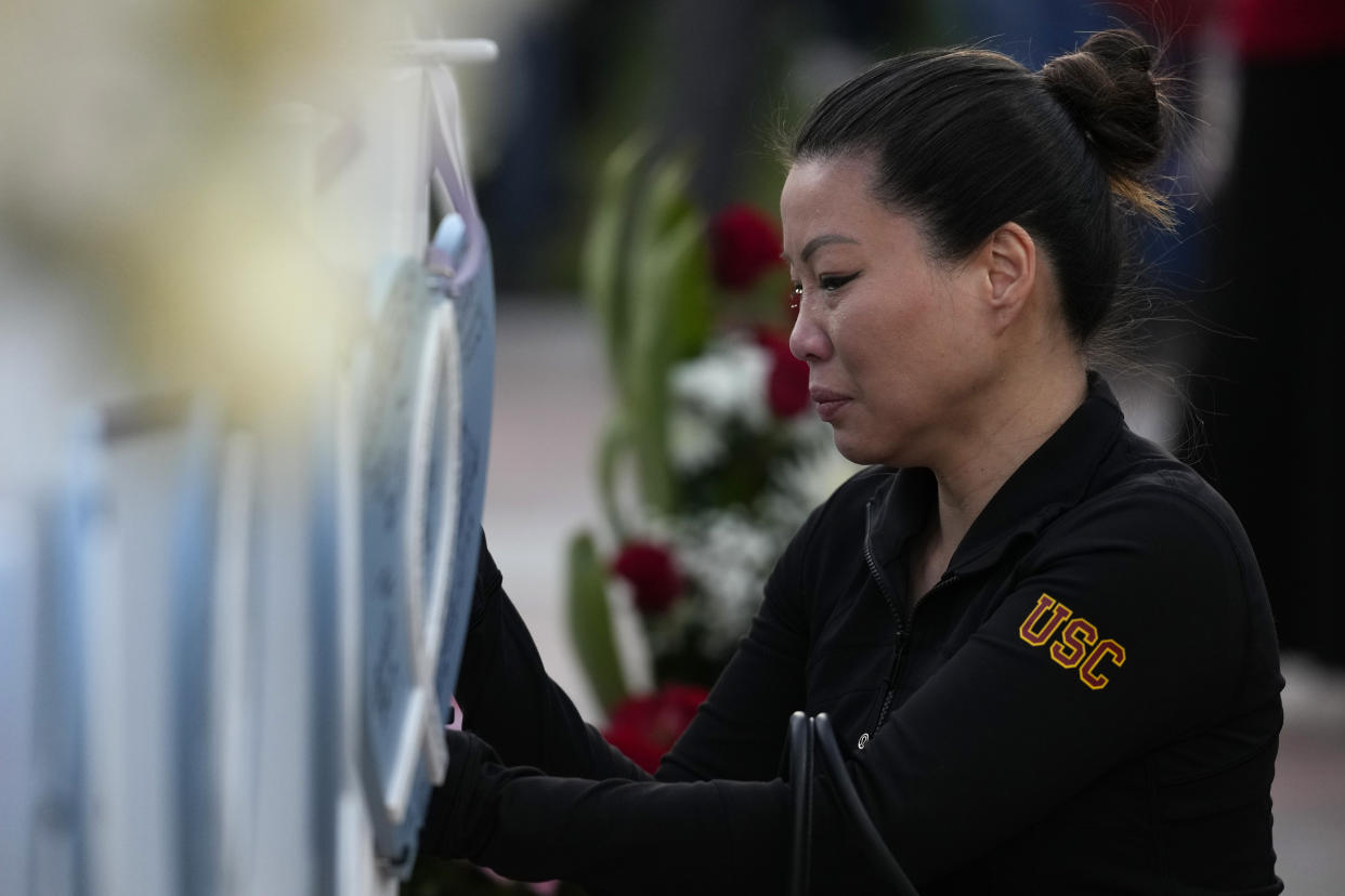 A woman writes a message on a wooden heart displaying the name of a victim at a vigil outside Monterey Park City Hall, blocks from the Star Ballroom Dance Studio on Tuesday, Jan. 24, 2023, in Monterey Park, Calif. A gunman killed multiple people at the ballroom dance studio late Saturday amid Lunar New Years celebrations in the predominantly Asian American community. (AP Photo/Ashley Landis)