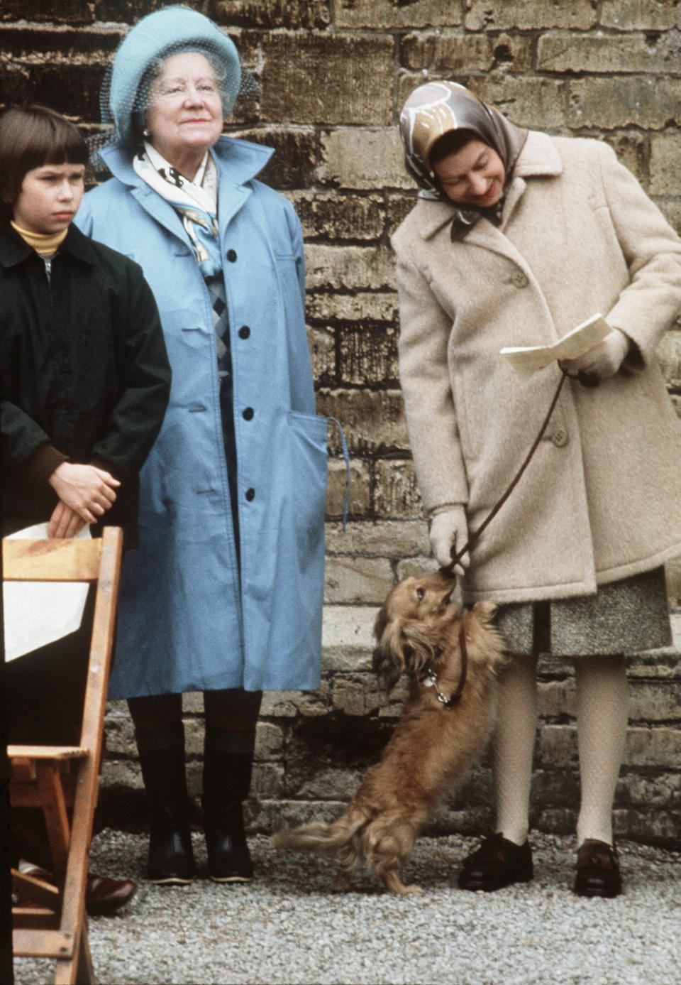 BADMINTON - APRIL 1:  Queen Elizabeth ll, standing with the Queen Mother and Lady Sarah Armstrong-Jones (now Sarah Chatto), pets one of her favourite dogs, a dorgi which is a cross between a corgi and a dachshund, at the Badminton Horse Trials in April 1976. (Photo by Anwar Hussein/Getty Images)