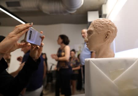 A woman takes a photograph of the artistic rendering of the head and face of a 13-year-old girl from the the prehistoric human species, Denisovan, based on technology developed by Hebrew University professor Liran Carmel and his team, in Jerusalem