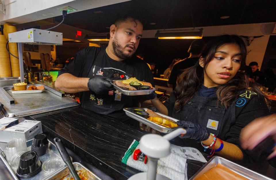 Los meseros Leslie Bustos y Rubén Ojeda apresurándose a servir algunos pedidos desde la cocina de Apocalypse BBQ.