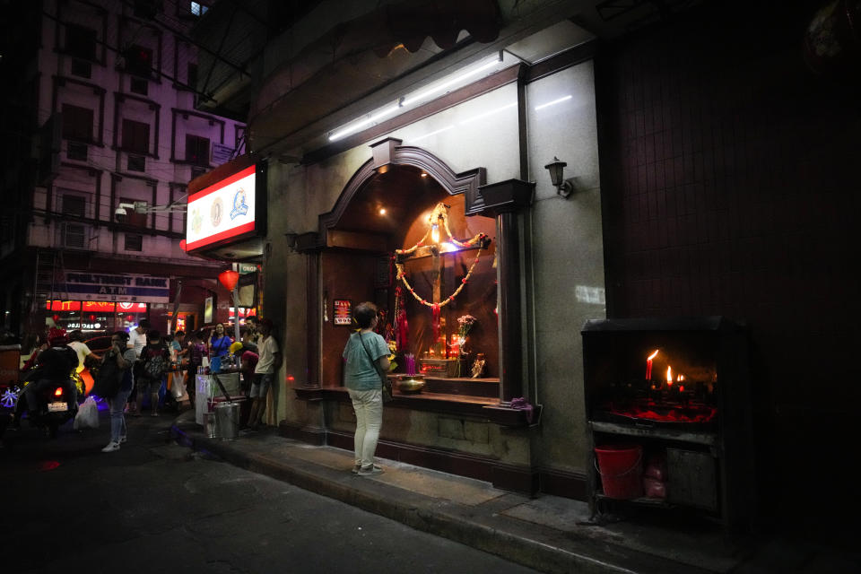 A woman offers prayers at a cross along a busy road at Binondo district, said to be the oldest Chinatown in the world, in Manila, Philippines on Tuesday Feb. 6, 2024, Crowds are flocking to Manila's Chinatown to usher in the Year of the Wood Dragon and experience lively traditional dances on lantern-lit streets with food, lucky charms and prayers for good fortune. (AP Photo/Aaron Favila)