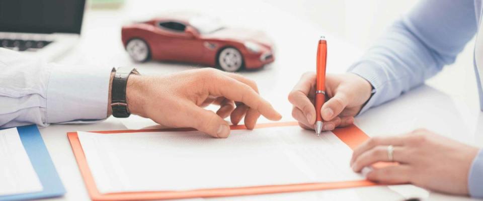 Woman signing a car insurance policy, the agent is pointing at the document