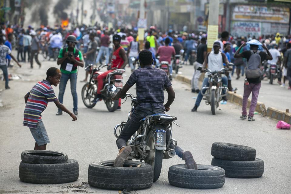 A motorcyclist uses his feet to drag tires into place for a barricade during a protest to demand the resignation of President Jovenel Moise in Port-au-Prince, Haiti, Saturday, Oct. 17, 2020. The country is currently experiencing a political impasse without a parliament and is now run entirely by decree under Moise. ( AP Photo/Dieu Nalio Chery)