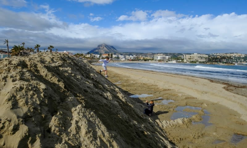 People walk past a huge sand shaft built to protect the Arenal Beach ahead of the upcoming storm "Gloria", in Javea near Alicante