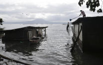 A man clears out volcanic ash from his roof at a lakeshore village where water has already reached their homes after Taal volcano'fs recent eruption in Agoncillo, Batangas province, southern Philippines on Saturday Jan. 18, 2020. The Taal volcano near the Philippine capital emitted more ash clouds Saturday, posing the threat of another eruption. (AP Photo/Aaron Favila)