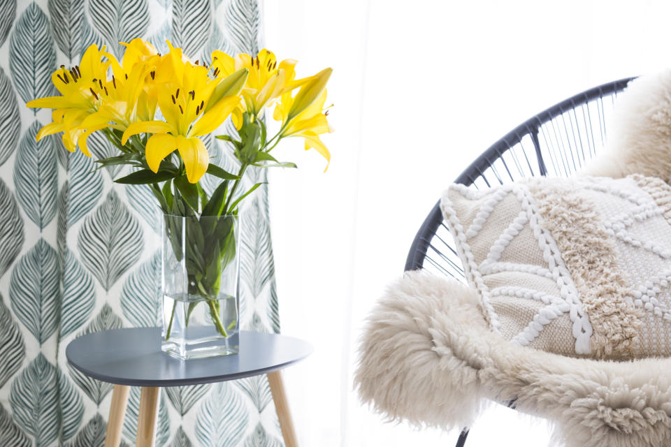 Comfortable chair with sheepskin and cushion on a white carpet in front of a high key window with vase of yellow lilies alongside