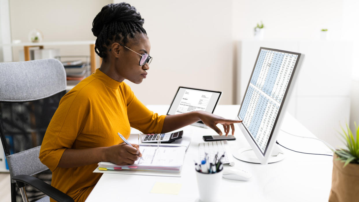  A person at a desktop computer working on spreadsheet tables. 