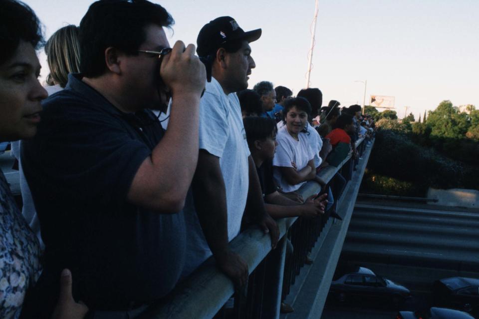 People watch the road below from a freeway overpass.