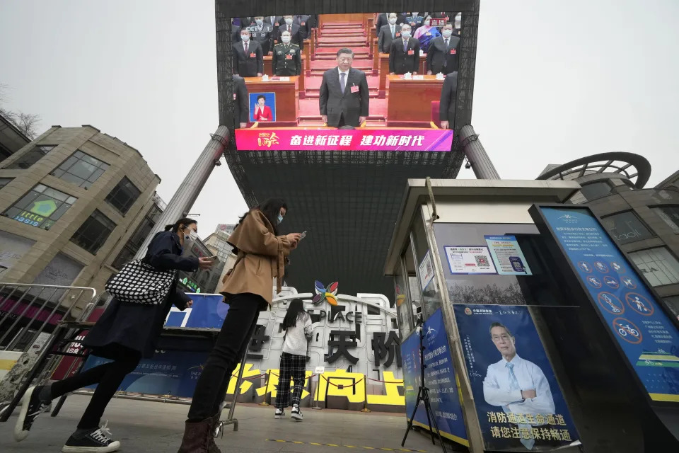 Women scan health check QR codes to enter a shopping mall as a large video screen shows Chinese President Xi Jinping during coverage of the closing session of China's National People's Congress (NPC) in Beijing, Friday, March 11, 2022. (AP Photo/Ng Han Guan)