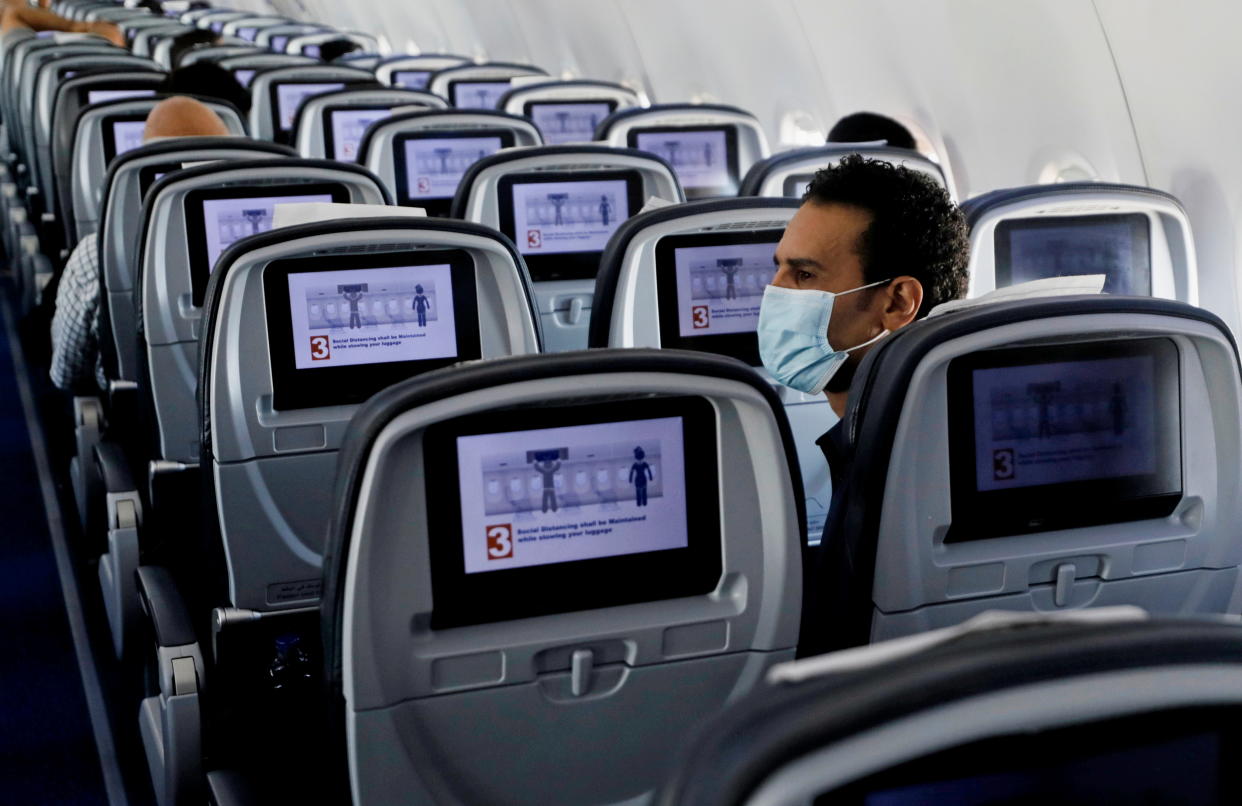 A traveler seated in a sparsely populated plane and wearing a surgical mask looks around him.