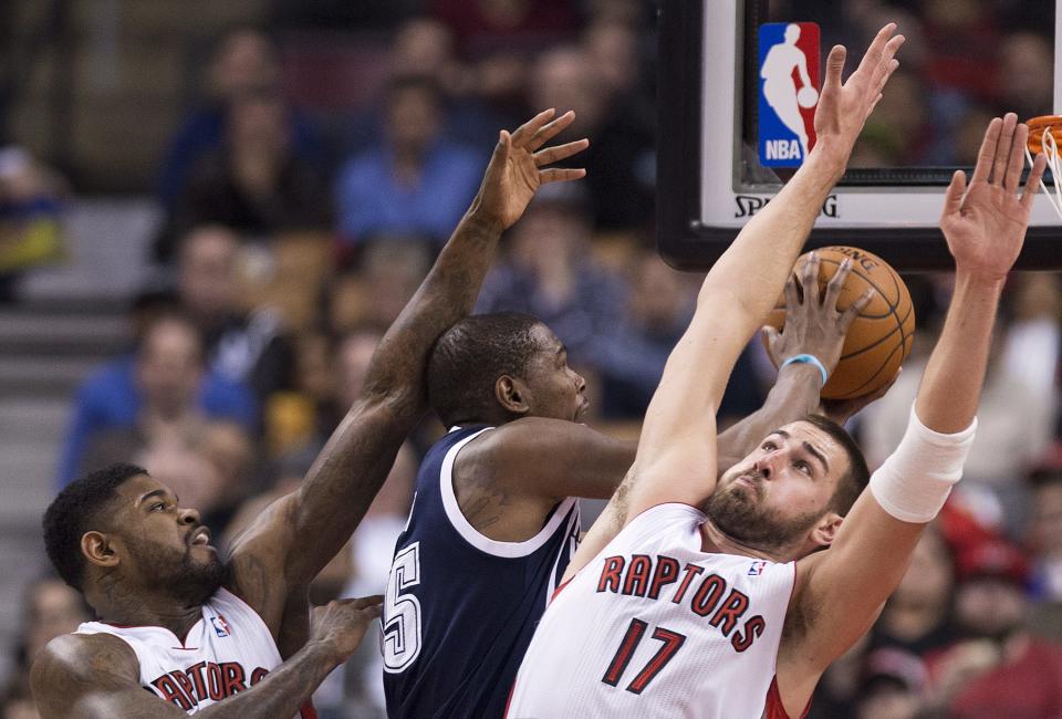 Toronto Raptors forward Amir Johnson, left, and Jonas Valanciunas, right, defend against Oklahoma Thunder forward Kevin Durant, center, during the first half of an NBA basketball game in Toronto on Friday, March 21, 2014. (AP Photo/The Canadian Press, Nathan Denette)