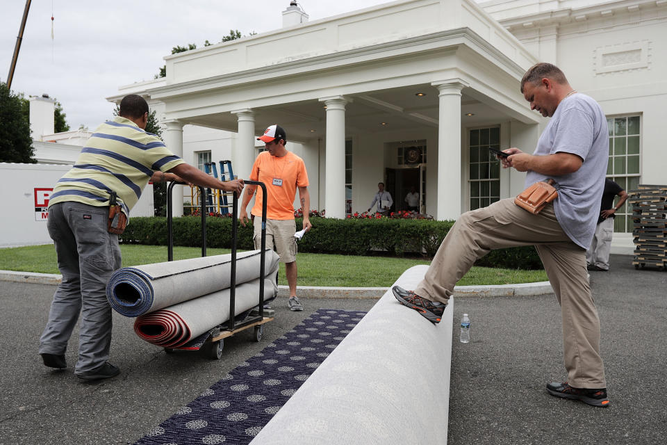 Workers measure and cut new carpeting in the driveway outside the West Wing.