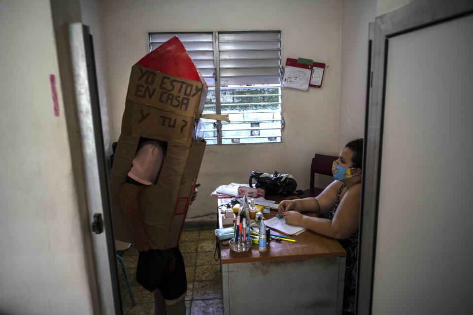 Retired nurse Feridia Rojas wearing a cardboard box as a protective measure against the spread of the new coronavirus, stops in for a friendly visit with the family doctor, in Havana, Cuba, Wednesday, July 8, 2020. The 82-year-old pensioner shuffles through the streets of Havana on shopping excursions wearing the cardboard box, with a handwritten message that reads in Spanish, "I'm home, and you?" (AP Photo/Ramon Espinosa)