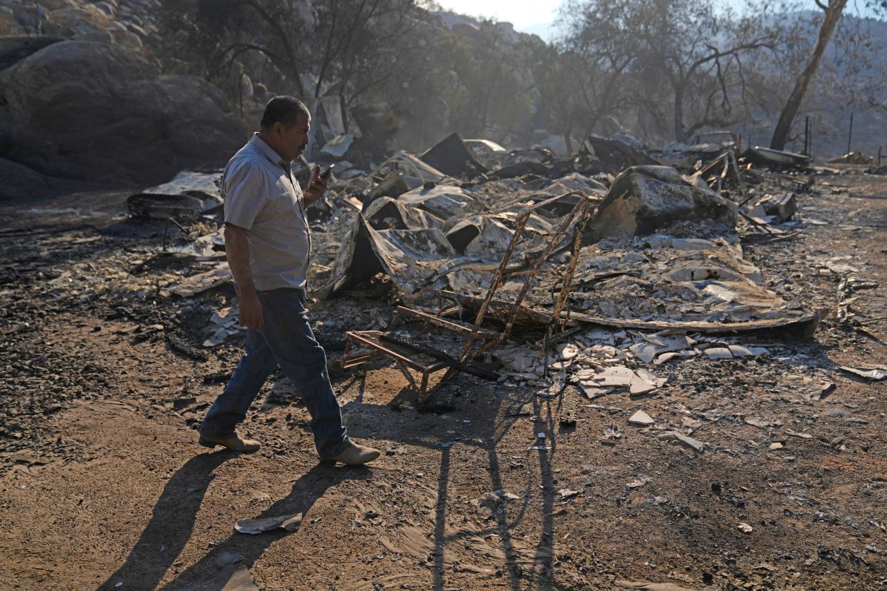 Luis Quinonez talks to a neighbor on the phone while surveying the damage to his property after the Highland Fire passed through Tuesday in Aguanga.