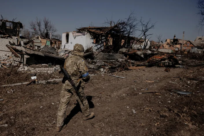 A soldier walks through a destroyed village.