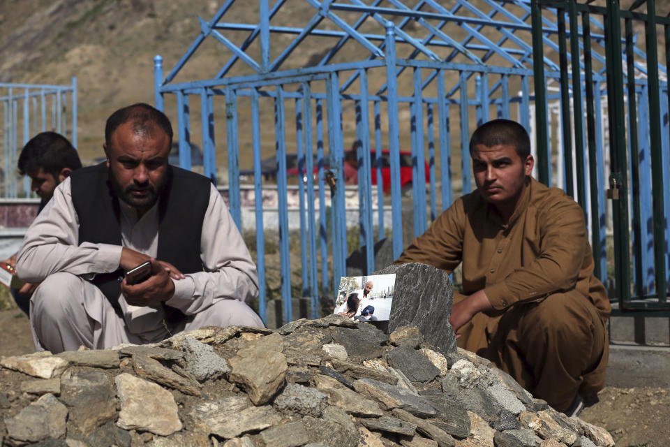 In this Wednesday, May 20, 2020 photo, members of the Aryubi family mourn over the graves of Dr. Yousuf Aryubi, in photo, and two of his siblings who lost their lives to COVID-19, in Kabul, Afghanistan. Dr. Aryubi's family assumed they just had a bad cold, as one after another, they came down with fevers and coughs -- all because one of the Afghan capital's main hospitals never told them the results of his coronavirus test. Their tragedy points to how a broken-down health system, slow government response and public attitudes have left Afghanistan deeply vulnerable to the global pandemic. (AP Photo/Rahmat Gul)