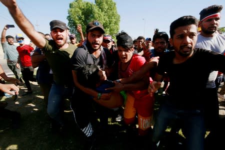 Men carry an injured demonstrator at a protest during a curfew, three days after the nationwide anti-government protests turned violent, in Baghdad