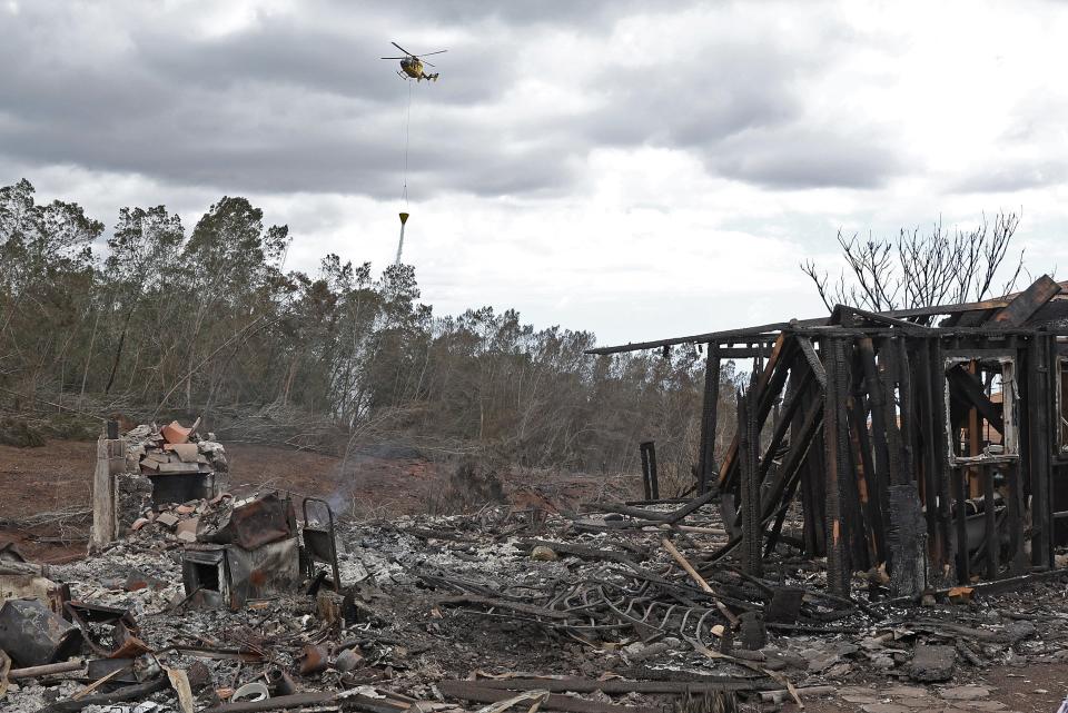 A firefighting helicopter drops water near a home that was destroyed by a wildfire on August 11, 2023 in Kula, Hawaii.