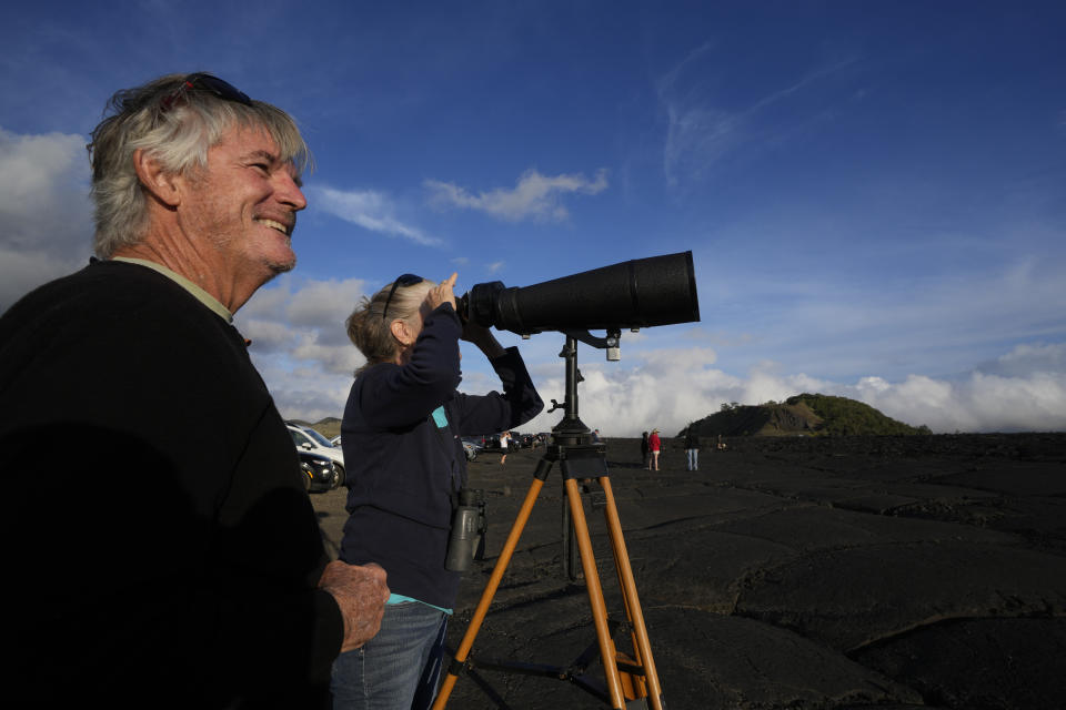 Mike, left, and Janice Hazen, of Ocean View, Hawaii, use a binocular to view the Mauna Loa volcano as it erupts Wednesday, Nov. 30, 2022, near Hilo, Hawaii. (AP Photo/Gregory Bull)