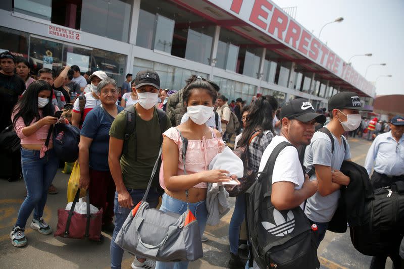 People wearing face masks wait to board a bus at a bus station after Peru's government deployed military personnel to block major roads, as the country rolled out a 15-day state of emergency to slow the spread of coronavirus disease (COVID-19), in Lima