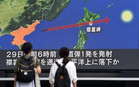Pedestrians watch the news on a huge screen displaying the trajectory of the missile that flew over Japan - Credit: AFP
