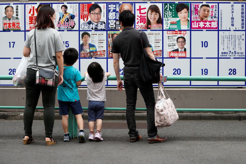 A family watches candidate posters, including current governor Yuriko Koike, for the Tokyo Governor election in front of a voting station amid the coronavirus disease (COVID-19) outbreak, in Tokyo